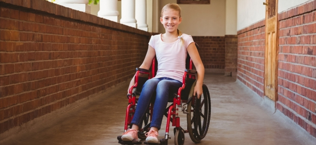A child is seen in a wheel chair with a school setting in the background