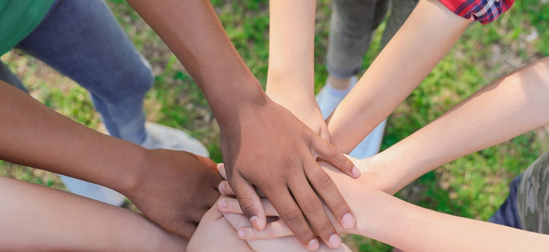 A group of people are seen putting their hands together of multiple ethnicity and cultures