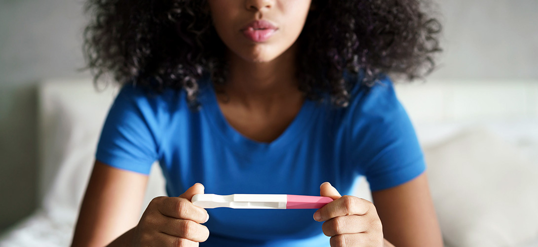A teenage girl sitting on a sofa holding a pregnancy test in her hands.