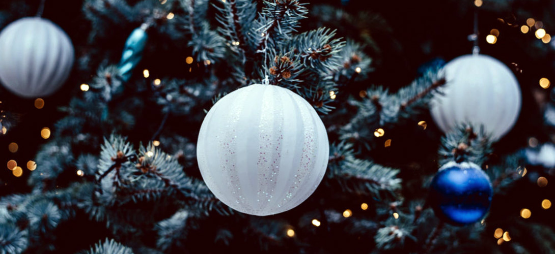 White and blue Christmas baubles hanging on the branches of a Christmas tree.