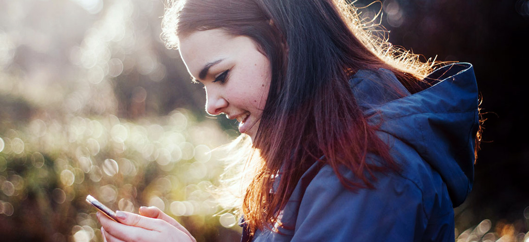Teenage girl smiling holding her mobile phone and looking at her screen.