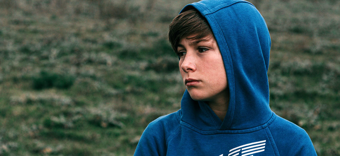 Young teenage boy wearing a hoodie looking off into the distance with a sad expression.