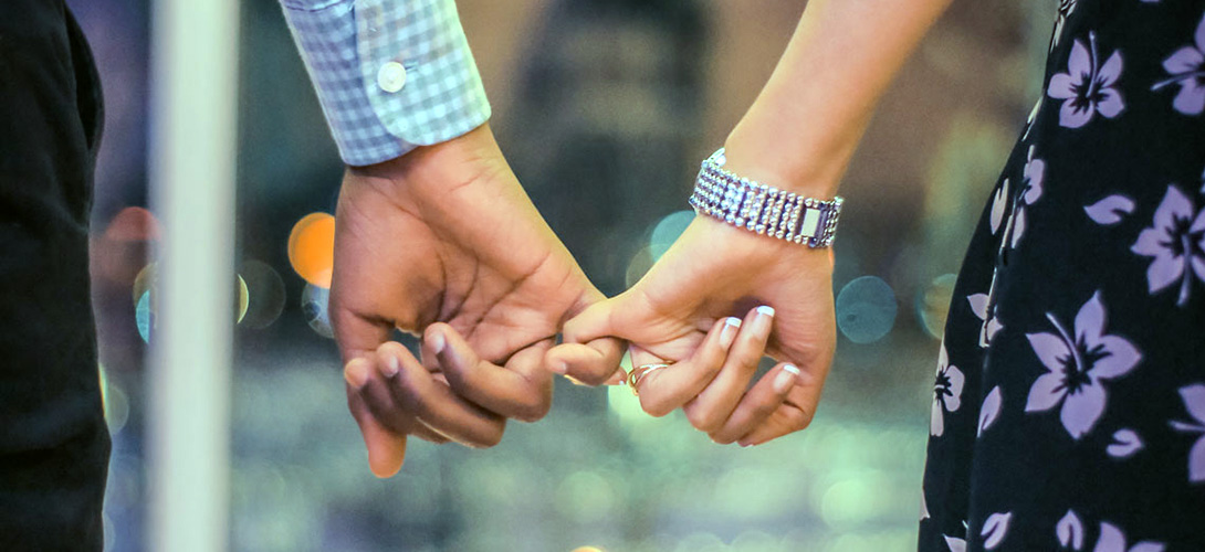 A close-up of a couples hands as they links little fingers.