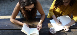 Two teenage girls sitting at a table outside doing their homework.