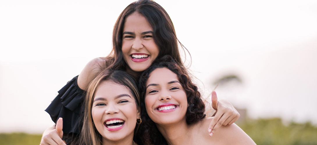 Three teenage girls who are friends laughing and smiling posing for a photo.