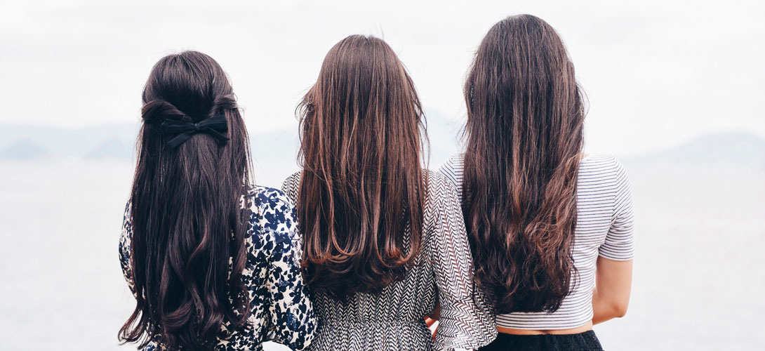 Three teenage girls with long hair standing with the backs to the camera.