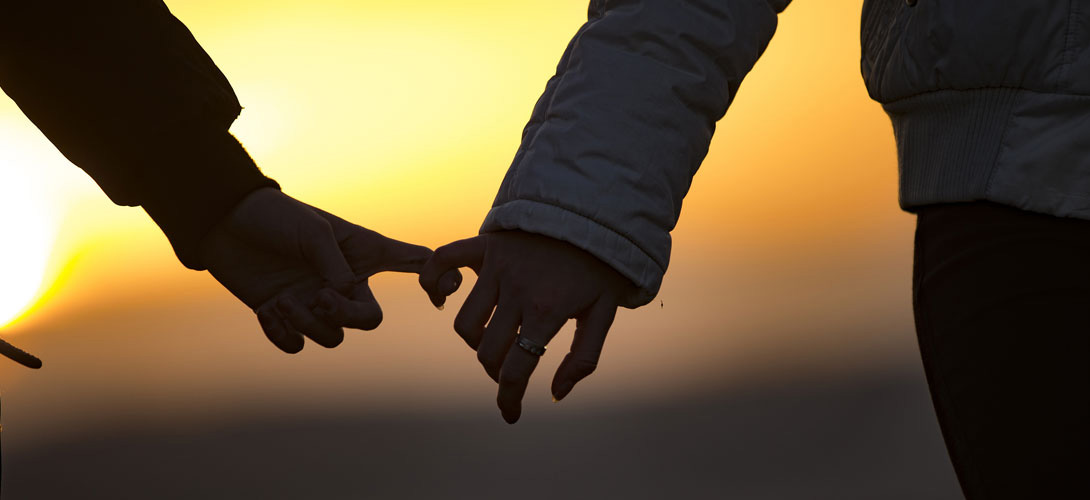 A young couple walking together in the sunset linking little fingers.