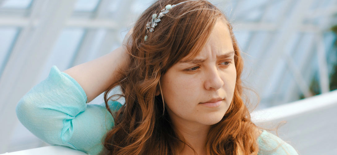 A teenage girl holding the back of her head with a puzzled look on her face.