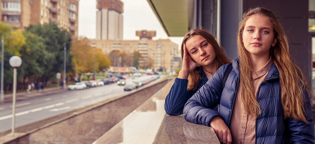 Two young girls standing out on an apartment balcony in a city centre.