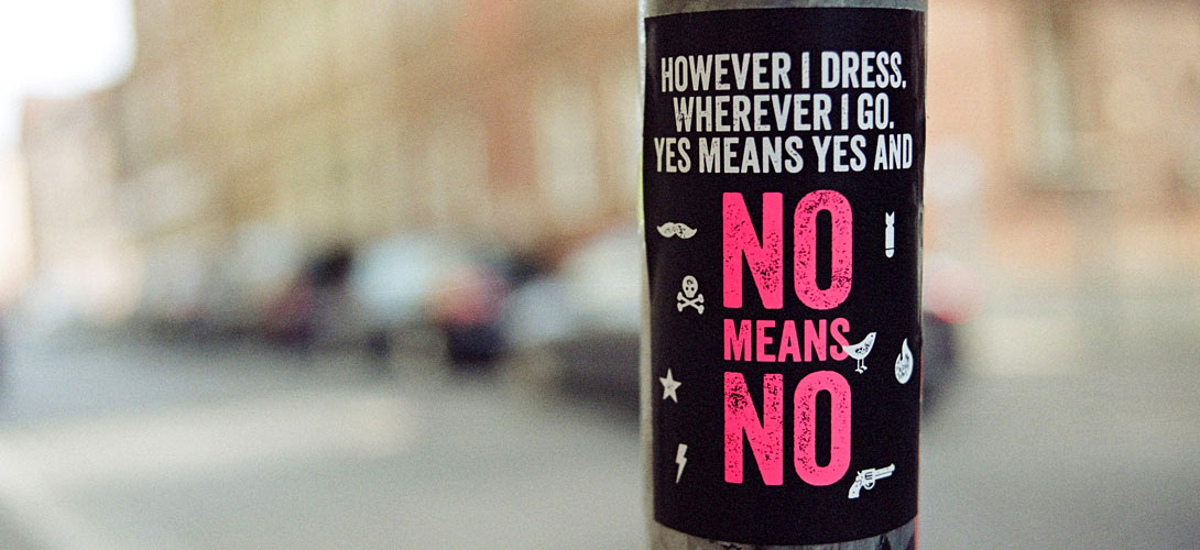 A black poster with white and pink writing spelling out the words "However I dress, wherever I go, yes means yes and no means no."