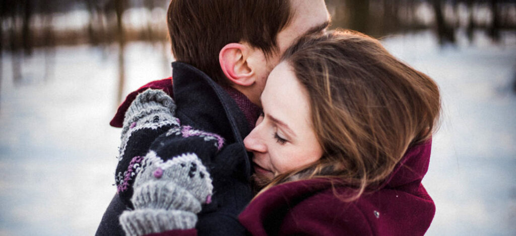 A couple hugging against a snowy background.