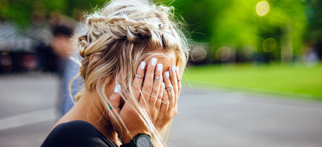 A close-up of a teenage girl covering her face with her hands.