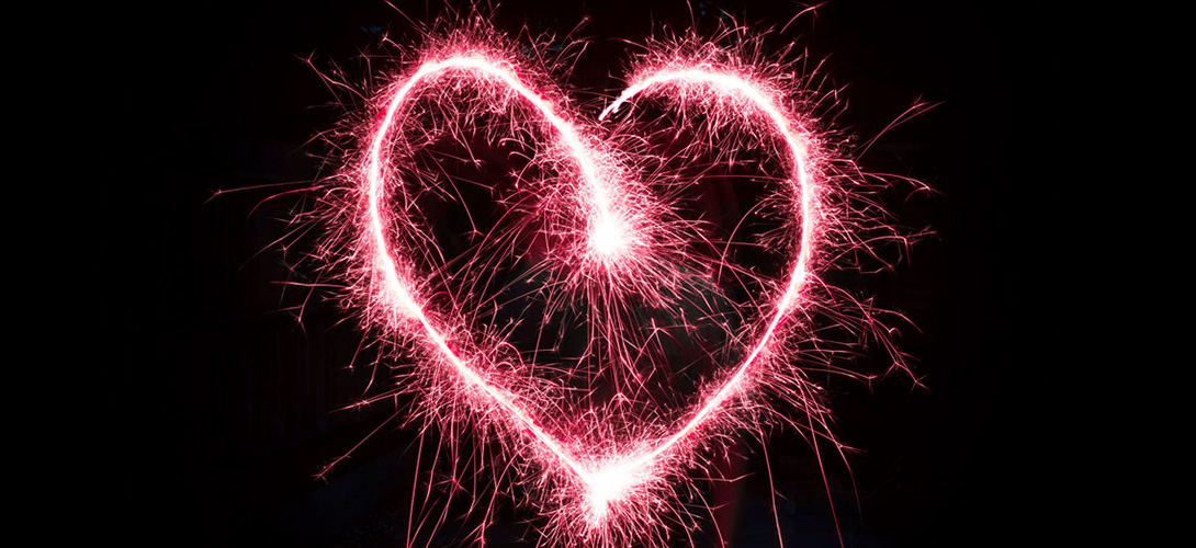 A heart shaped pink firework against a black night sky.