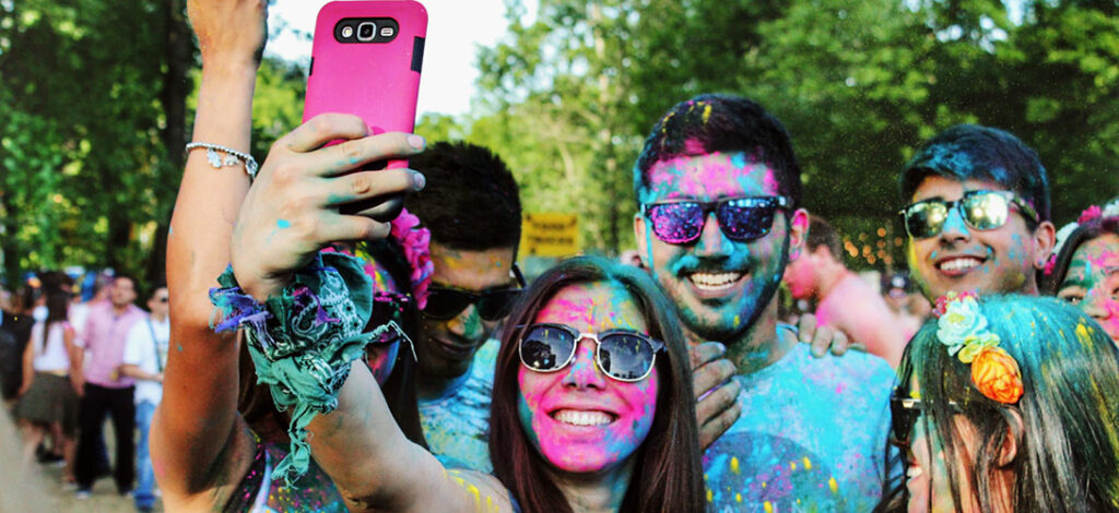 A group of young people covered in coloured powdered taking a group selfie.