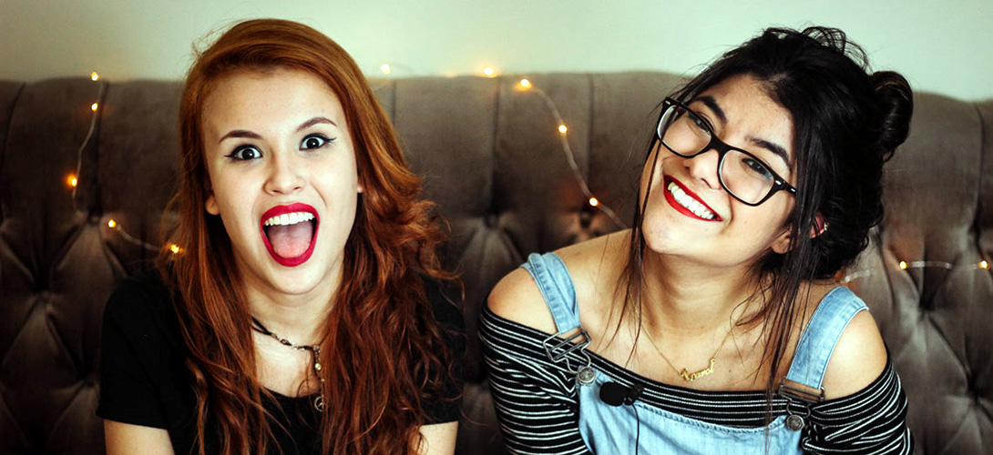 Two teenage girls sitting on a sofa smiling and laughing.