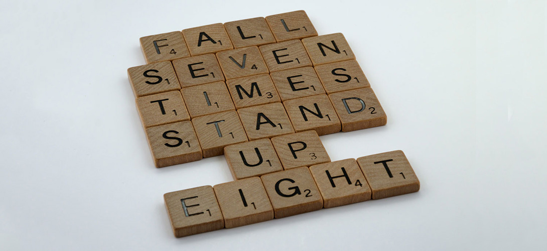 Wooden scrabble letters against a white background spelling out the words "fall seven times stand up eight".