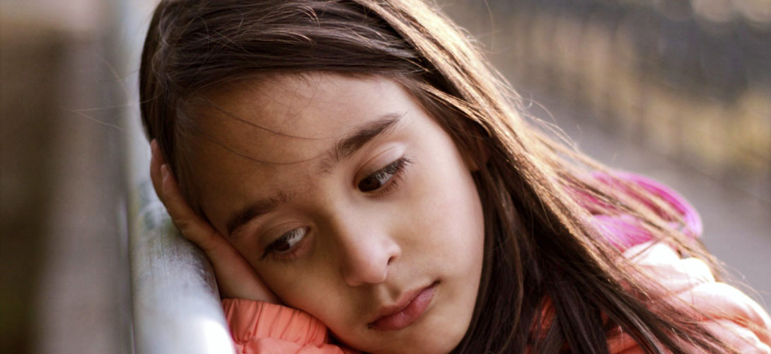 Close-up of a young girl looking sad, she is leaning against a handrail leaning her face against her hand.