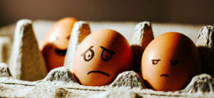 A cardboard egg carton with eggs showing different facial expressions such as worry, laughter and a frown drawn with a black marker.