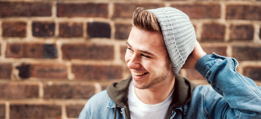 A older teenage boy standing against a brick wall looking to his right, smiling and laughing.
