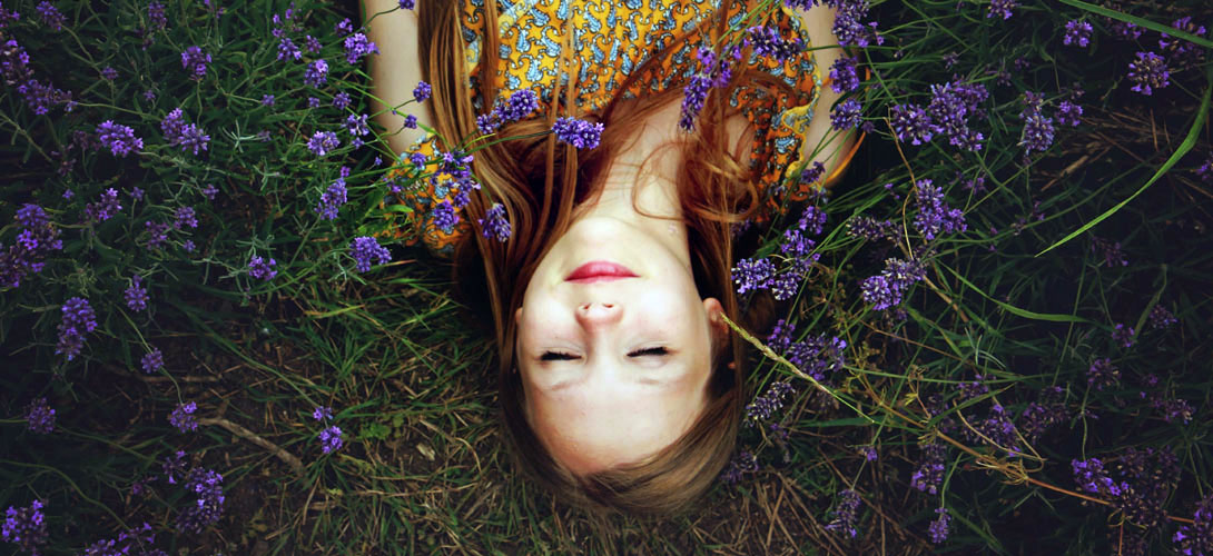 A close-up of a girl with long hair and eyes closed, lying upside down in a field of flowers.