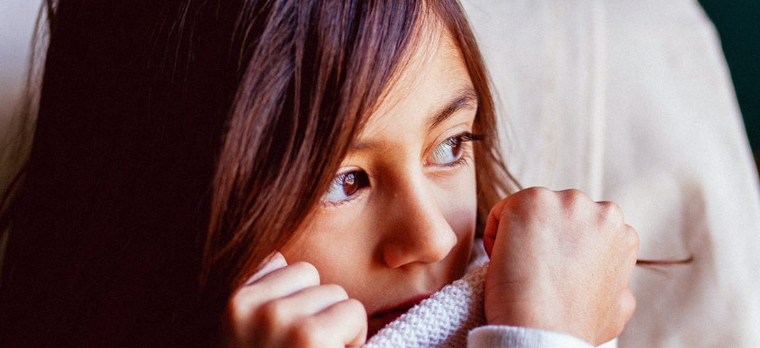 A close-up of a girl looking to the left while she pulls her jumper up to cover her mouth.