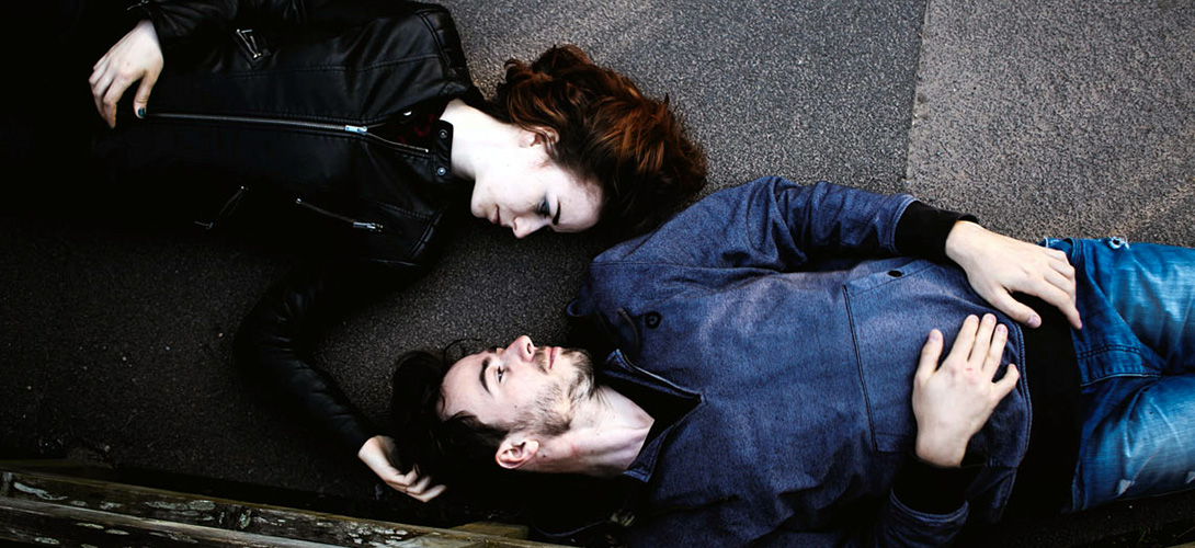 A young woman and man lying face to face on the ground.