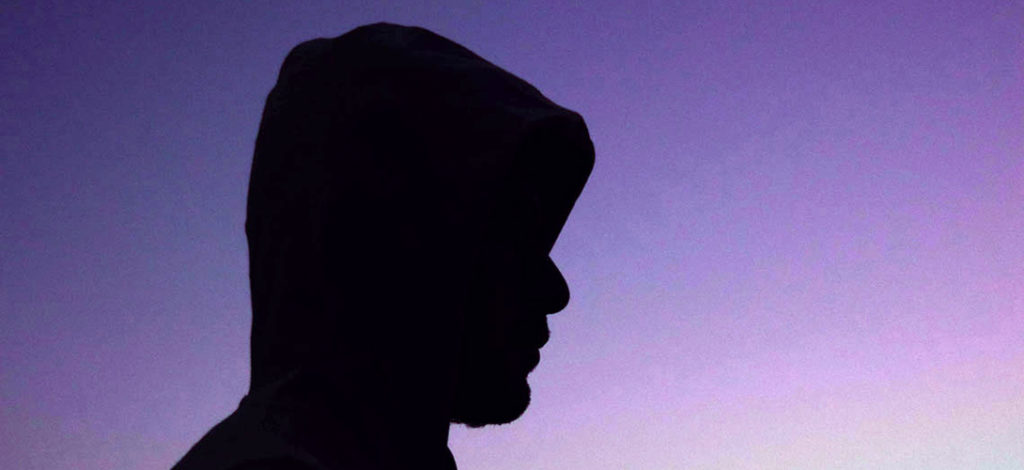 Silhouette of a teenage boy with his hoodie pulled up over his head set against a fade purple haze background.