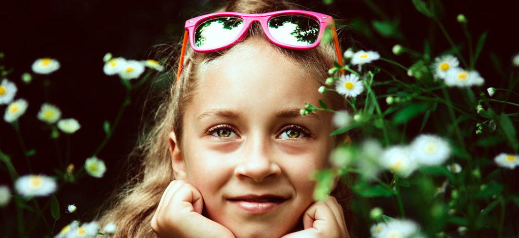 A close-up of a girl with sunglasses sitting on her head a smiling sitting amongst daisies.