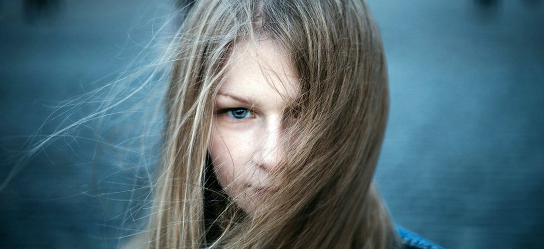 A close-up of a young girl looking straight ahead with her hair swept across her face.
