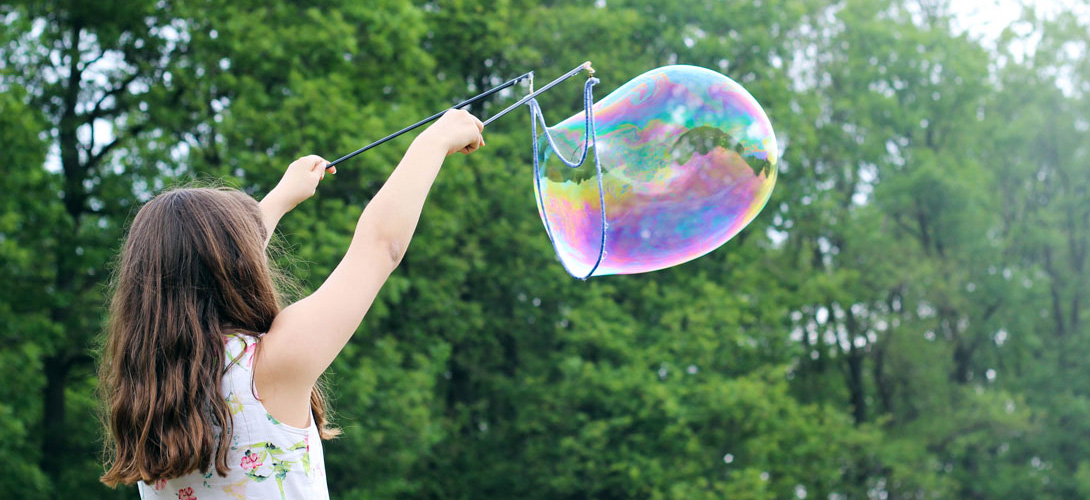 A young girl using a two sticks and string to create a giant bubble.