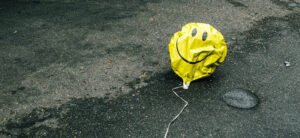 Deflated yellow smiley face balloon lying on the ground.