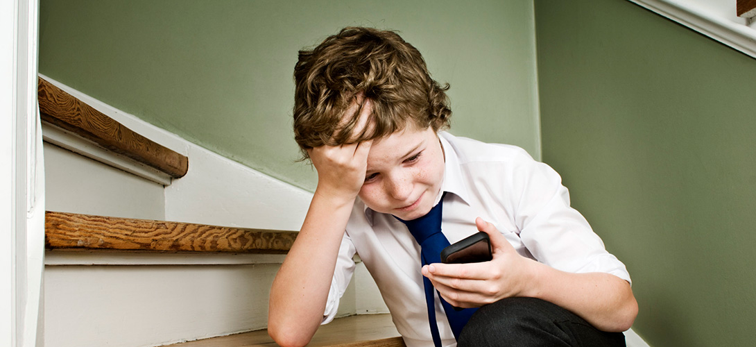Young boy, 10 years old, in tears after receiving a threatening text message on his mobile phone. Young boy 10 years with a strained expression on his face.