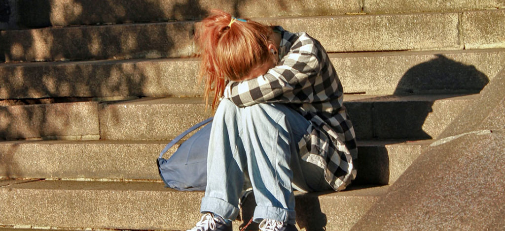 A teenage girl sitting on steps, her knees are bent and she is resting head in her arms leaning across her knees.